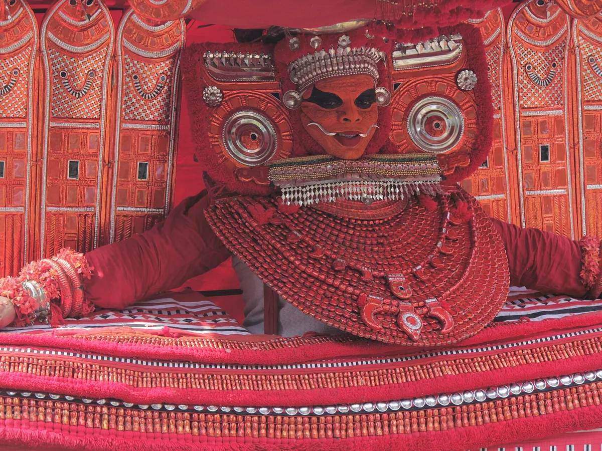 A Theyyam performer in elaborate red ritual costume and face makeup