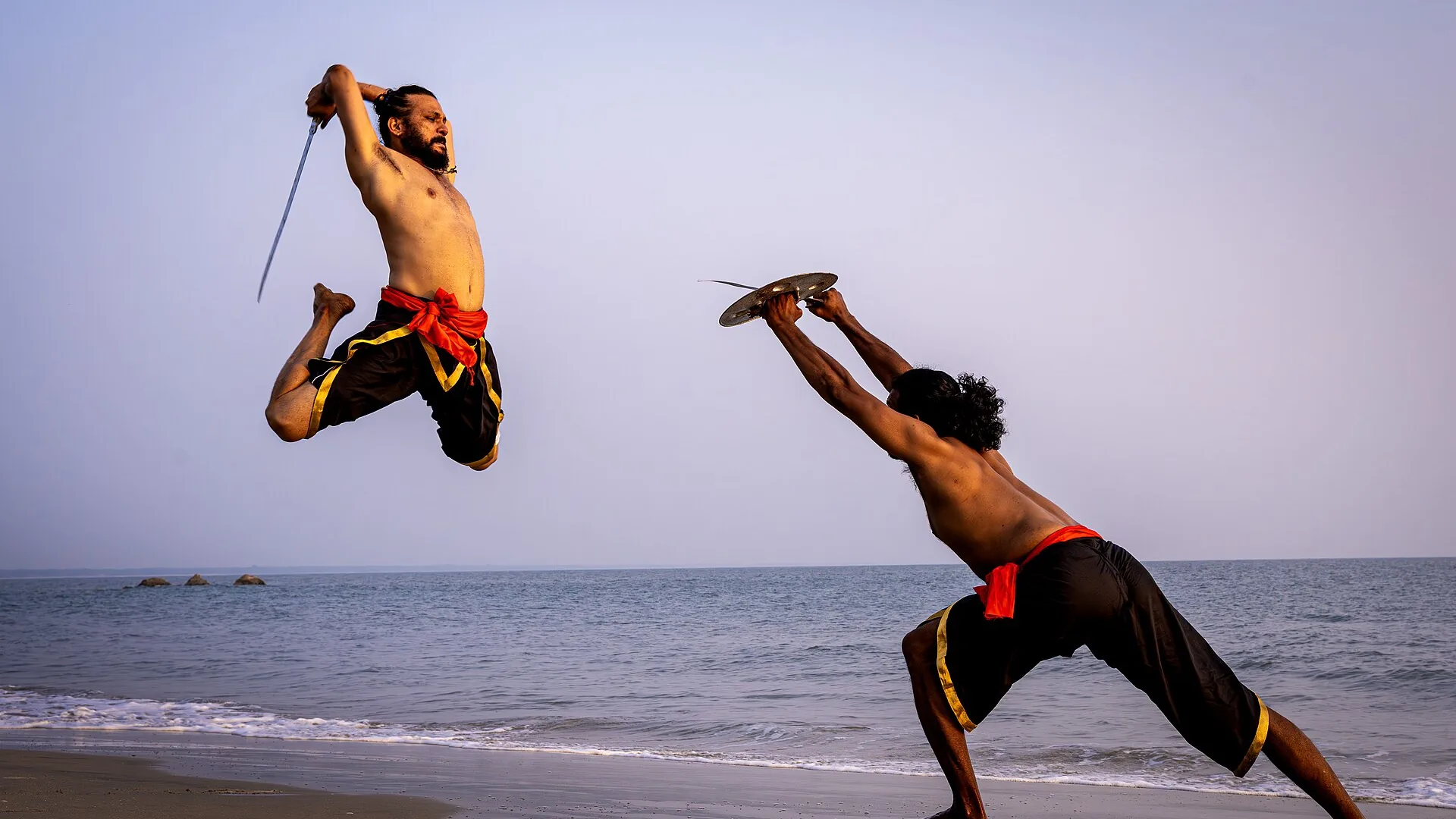 A Kalaripayattu practitioner in Kerala performing a weapons sequence with a curved sword and shield inside a traditional kalari training pit